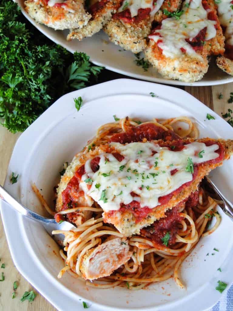 Top view of baked chicken parmesan on top of spaghetti noodles with a bite of chicken on fork. 