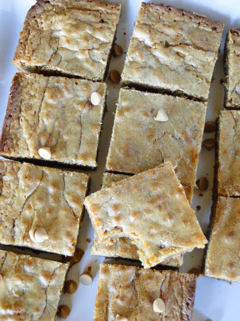 Top view of butterscotch blondies cut into squares with bite taken out of one bar sitting on top.