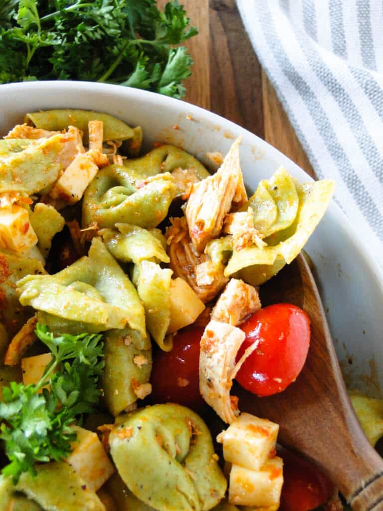 Close up view of chicken tortellini salad in white round bowl with wood serving spoon.