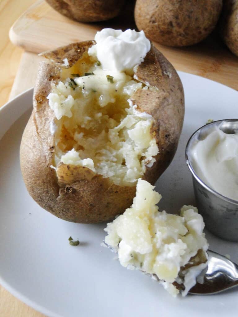 Instant pot potato on plate with dollop of sour cream and bite on a fork with extra sour cream on the side. 