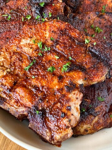 Close up of grilled spiced pork chops on white oval platter.