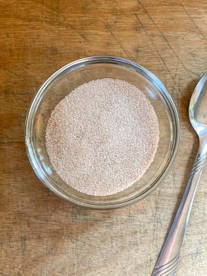 Cinnamon sugar topping for mini muffins in small bowl with spoon next to it.