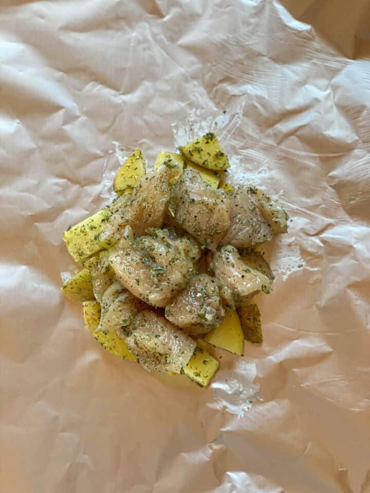 Chicken pieces placed on top of potatoes on foil.