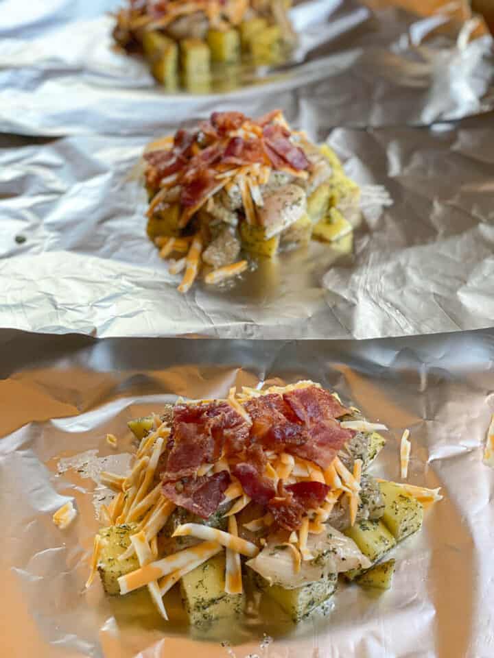 Pieces of potatoes and chicken topped with shredded cheese and cooked bacon pieces on foil.