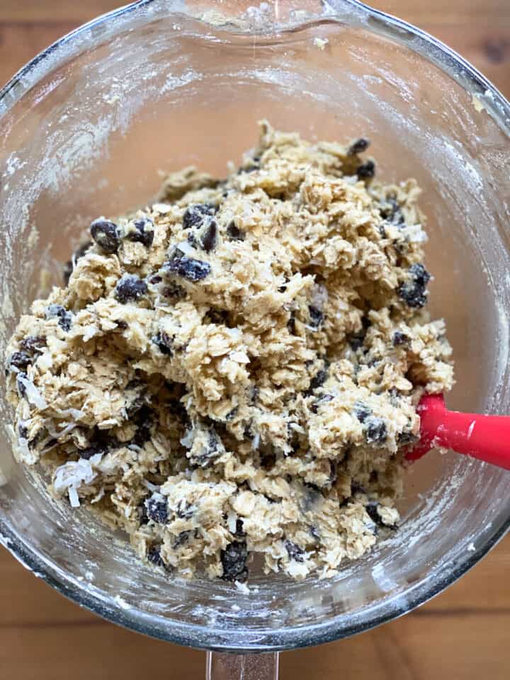 Cookie dough completely mixed together in glass mixing bowl with red spatula.