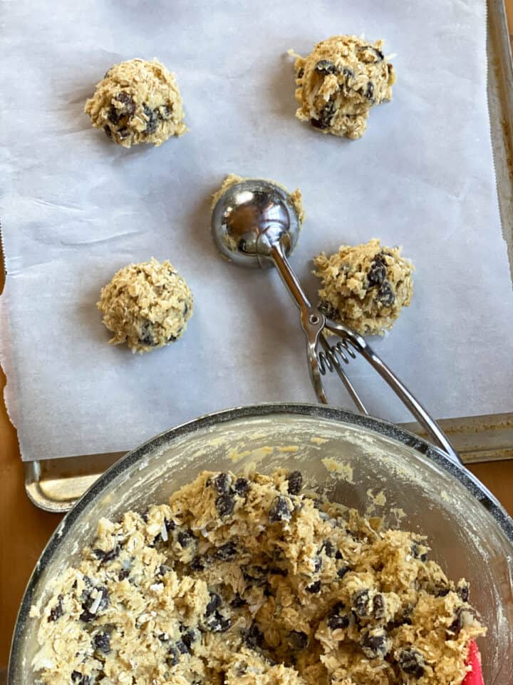 Cookie dough scooped on parchment lined cookie sheets with metal scooper.