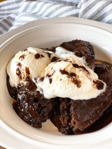 Crock pot chocolate lava cake dished into a white bowl topped with vanilla ice cream.
