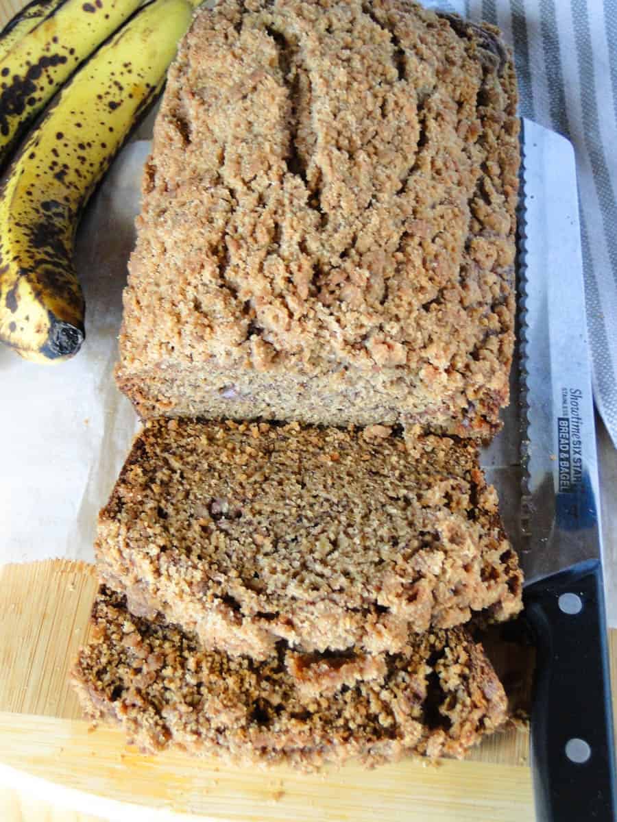 Top view of crumb topped banana bread with 2 slices on board.