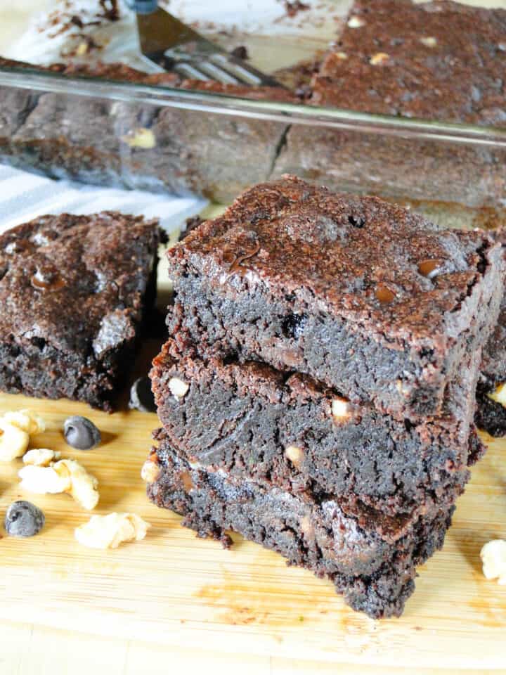 Dark chocolate walnut brownie slices stacked 3 high on board.