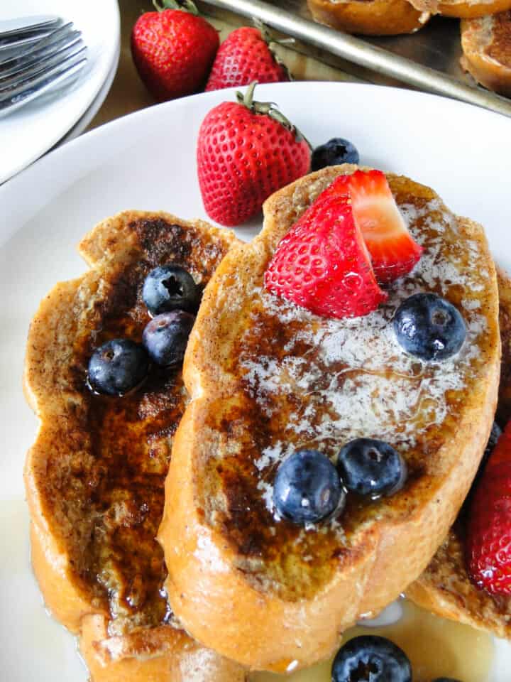 Close up view of classic french toast on plate with berries and syrup.