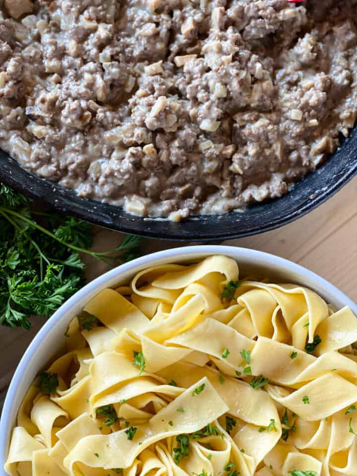 Easy ground beef stroganoff in skillet next to bowl of egg noodles.