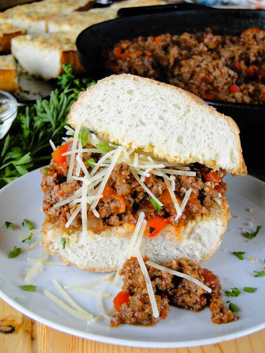 Side view of Italian sloppy joe on white round plate topped with shredded parmesan cheese.