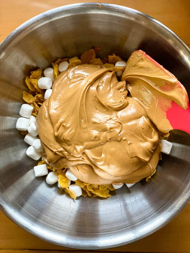 Butterscotch sauce added to large bowl with corn flakes and mini marshmallows.