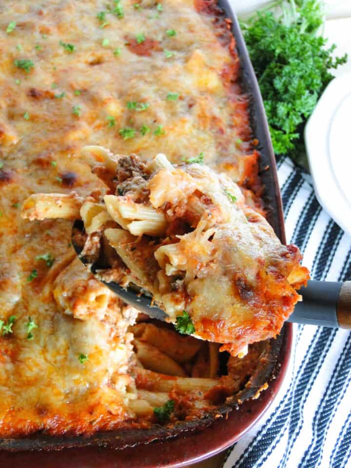 Baked penne casserole in baking dish with scoop on serving spoon.