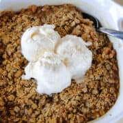 Easy peach crisp is white baking dish topped with 3 scoops of vanilla ice cream.