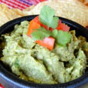 Easy homemade guacamole in bowl topped with diced tomatoes and cilantro leaves.
