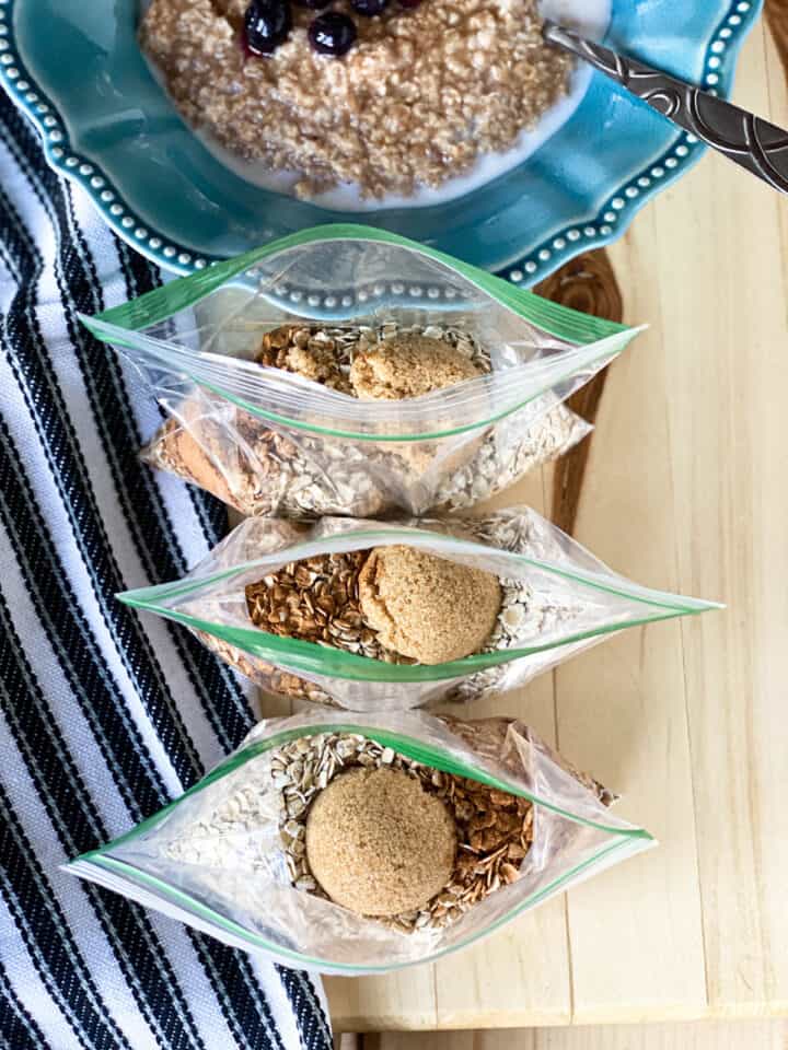 Homemade instant oatmeal prepped in zip top bags sitting in front of a bowl full of cooked oatmeal.