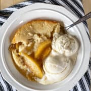 Top view of peach cobbler in white bowl with 2 scoops of vanilla ice cream and spoon.