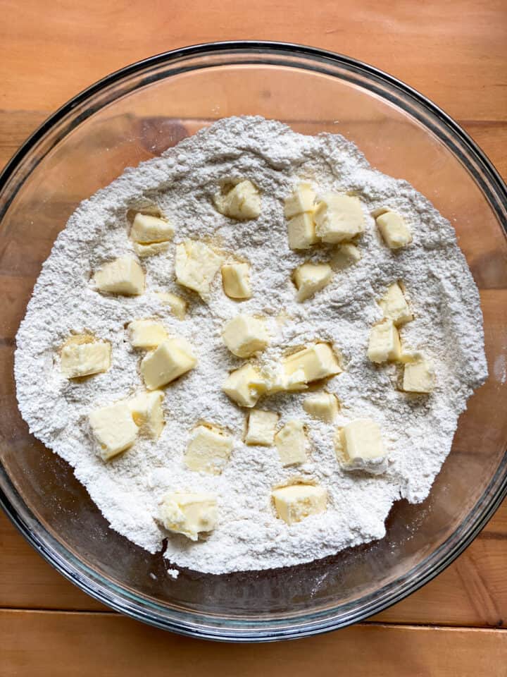 Dry ingredients in large glass bowl with cubes of butter.