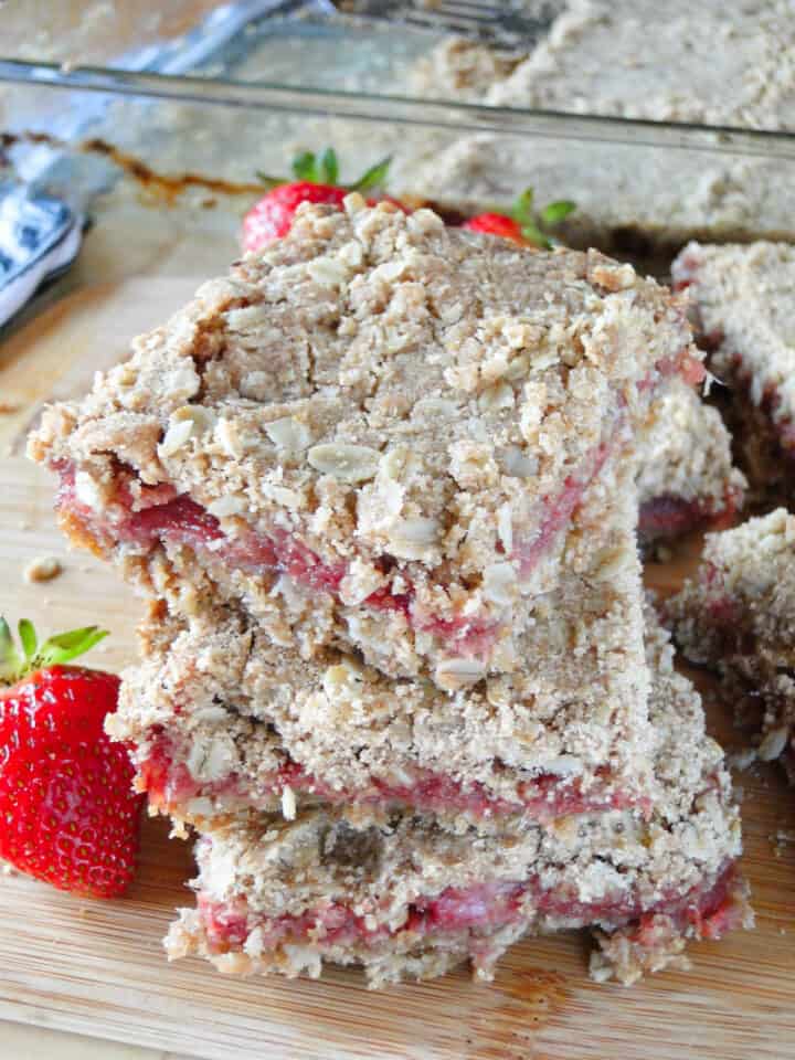 Sliced strawberry rhubarb oat bars stacked 3 high in front of baking dish of bars.
