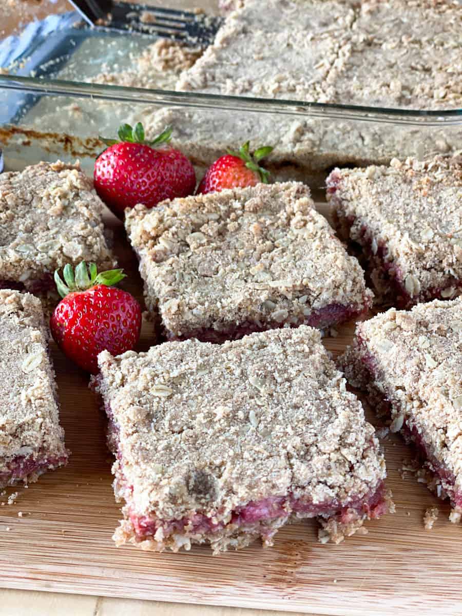 Strawberry rhubarb oat bars sliced into squares and on a board in front of the dish of bars.