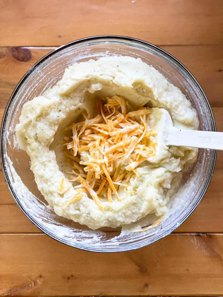 Shredded cheese added to the mashed potatoes in large bowl with spatula.