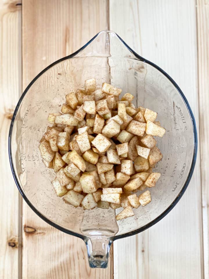 Apples and cinnamon mixed together in glass mixing bowl.