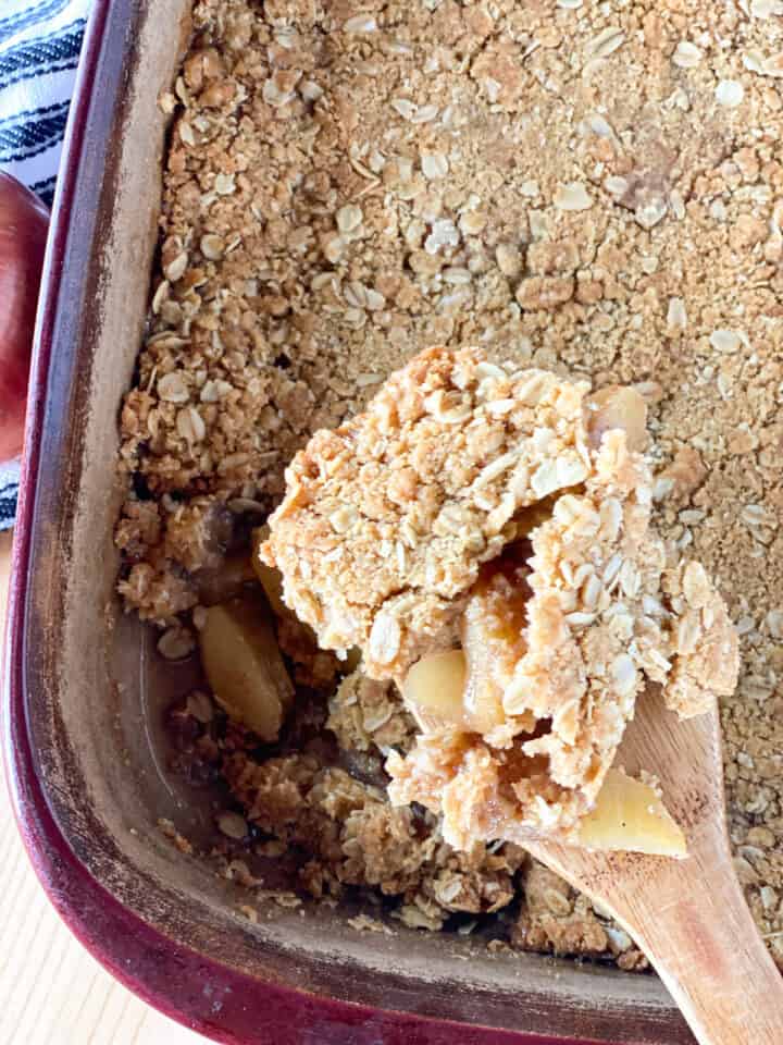 Easy apple crisp in baking dish with wooden spoon scooping out a serving.