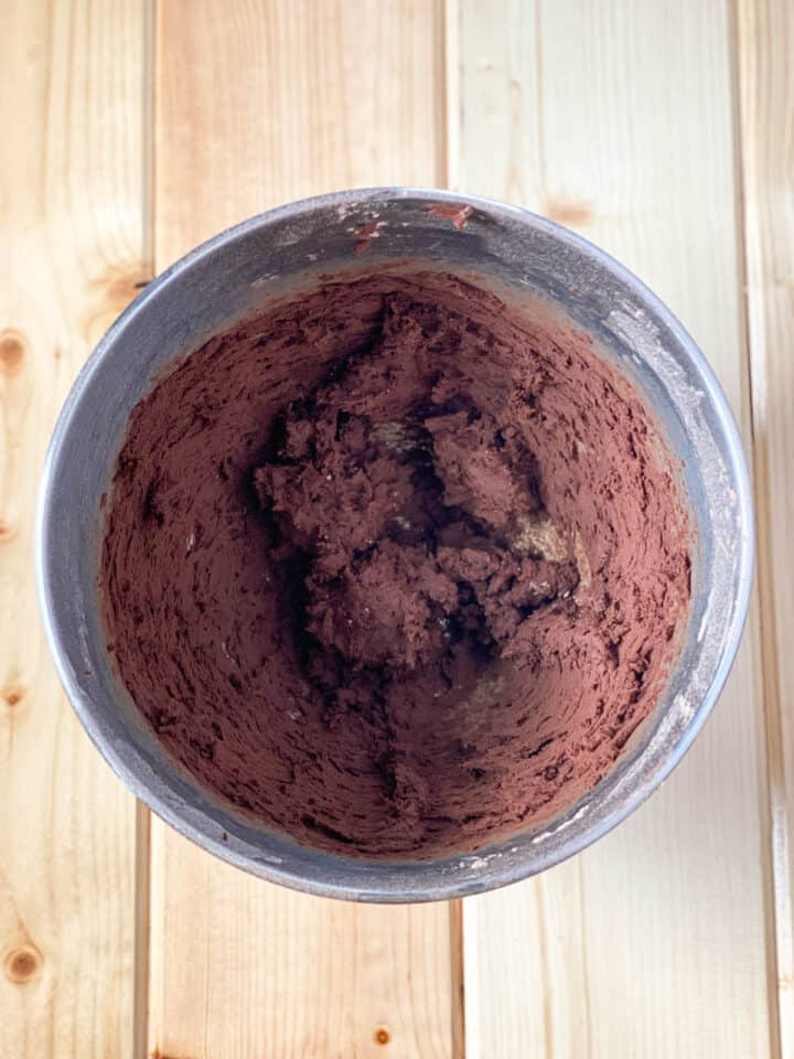 Cocoa powder added to butter for frosting in mixing bowl.