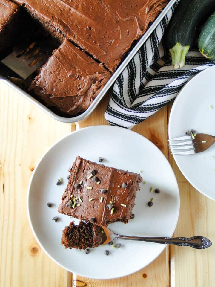 Top view of chocolate zucchini cake in cake pan and slice on plate with bite on fork.