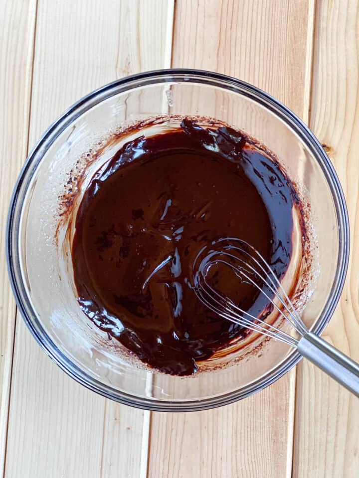 Cocoa powder and melted butter combined with whisk in glass bowl.