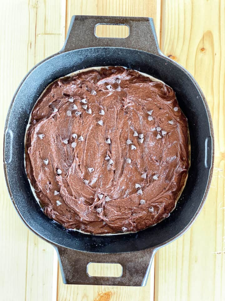 Brownie batter spread into skillet topped with extra chocolate chips.