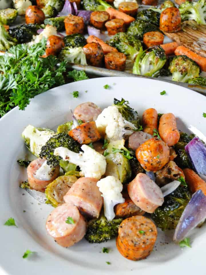 Side view of sausage and vegetables on plate in front of sausage sheet pan dinner.