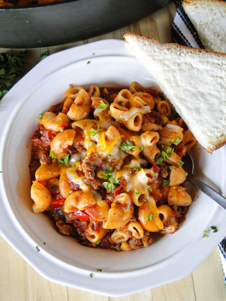 Easy skillet goulash served in white round bowl with half piece of buttered bread on the side.