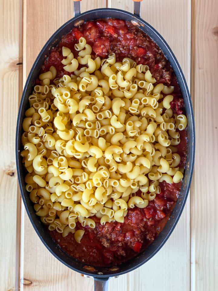 Raw macaroni added to tomato and beef mixture in skillet.