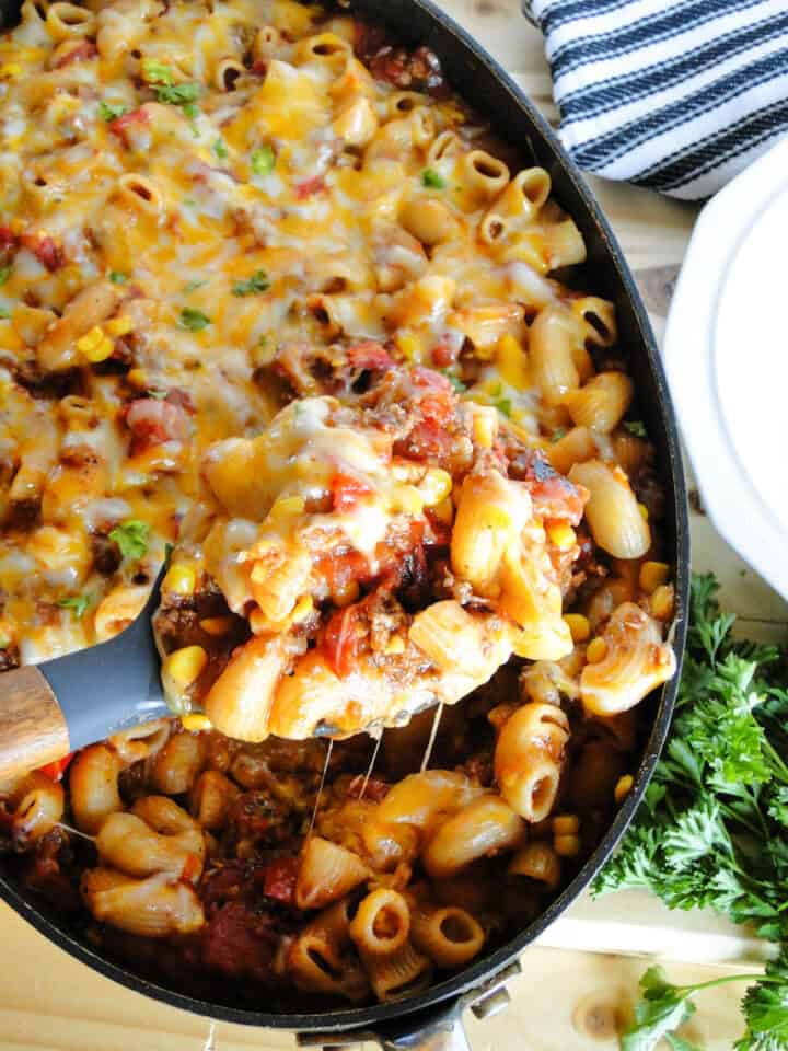 Easy skillet goulash being served out of skillet with large wood serving spoon.