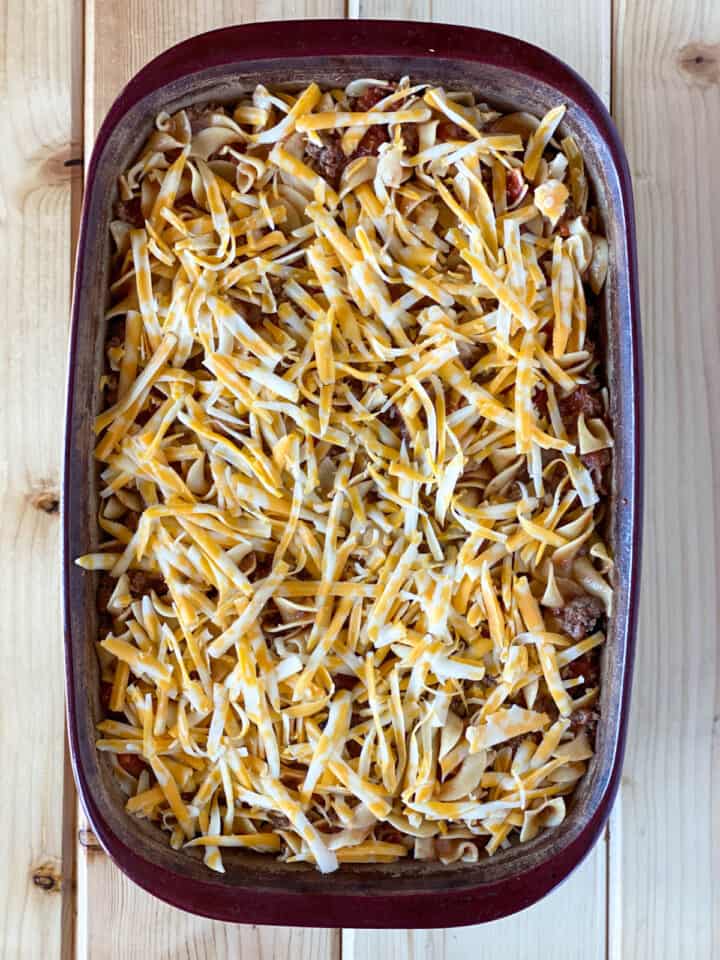 Cheese added to top of cooked pasta, beef and sauce in casserole dish.