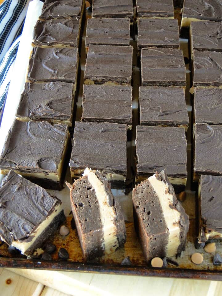 Sliced peanut butter brownie bars on sheet pan with 2 bars on their side showing pretty layers.