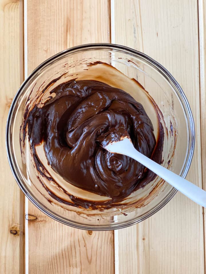 Chocolate ganache topping in small bowl with spatula.