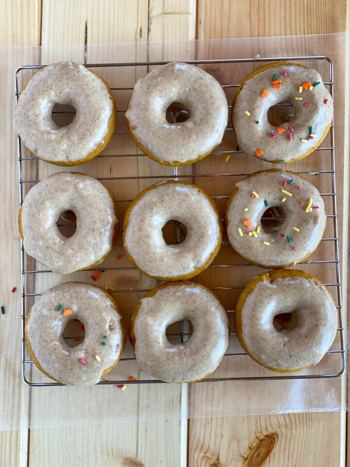 Frosted baked pumpkin donuts with sprinkles on wire rack.