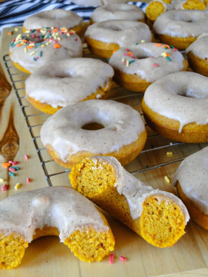 Side view of baked pumpkin donuts on wire rack with one donut cut in half showing fluffy inside.