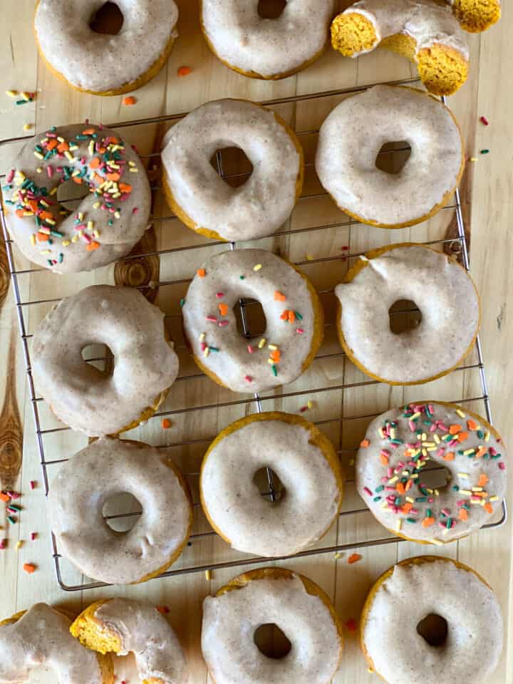 Baked pumpkin donuts with cinnamon glaze and sprinkles on wire rack.