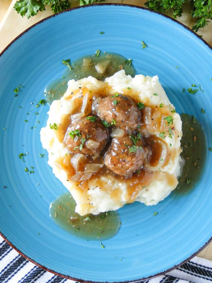 Top view of Salisbury Steak Meatballs served over mashed potatoes on blue round plate.