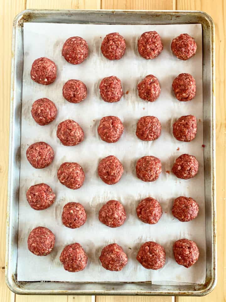 Rolled meatballs on parchment lined sheet pan.