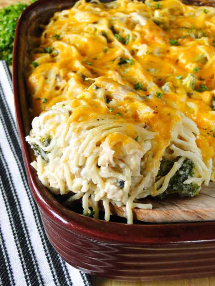 Chicken spaghetti bake being served out of casserole dish with wooden spatula.
