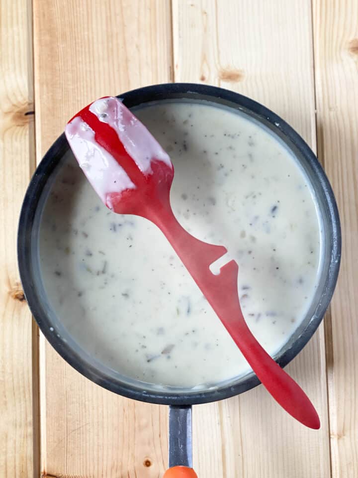 Béchamel sauce in sauce pan with red spoon showing thickness.