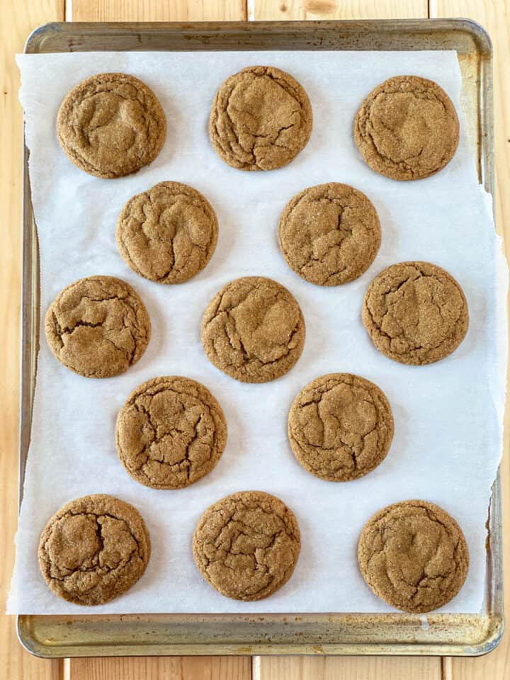 Baked chew molasses cookies on cookie sheet.