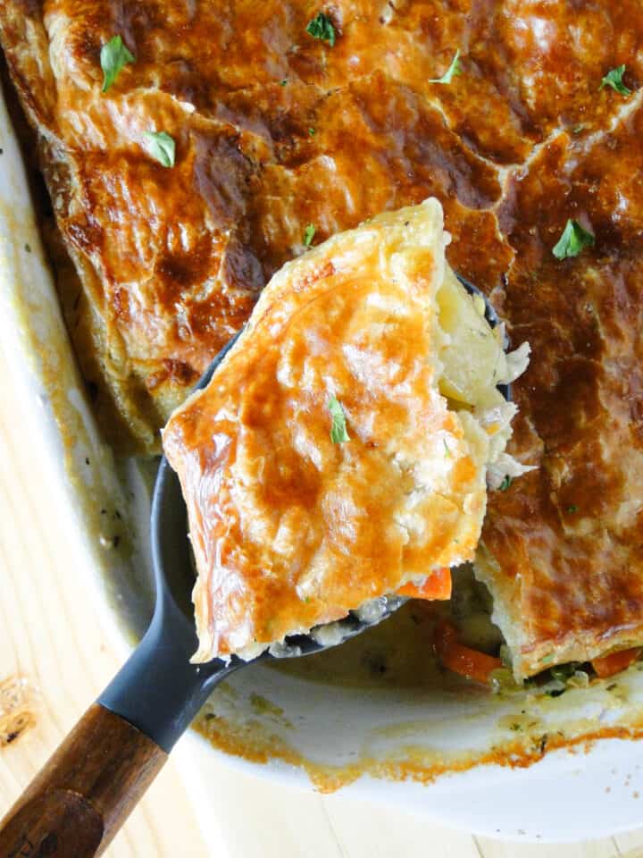 Turkey pot pie with puff pastry in casserole dish with scoop on wooden serving spoon.