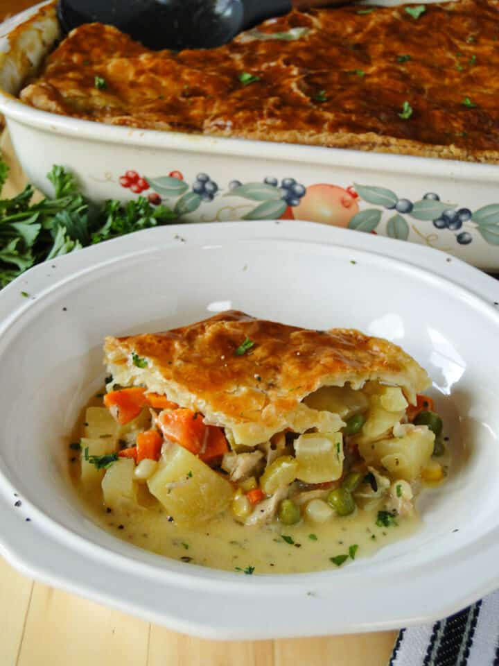 Side view of turkey pot pie with puff pastry in white round bowl.