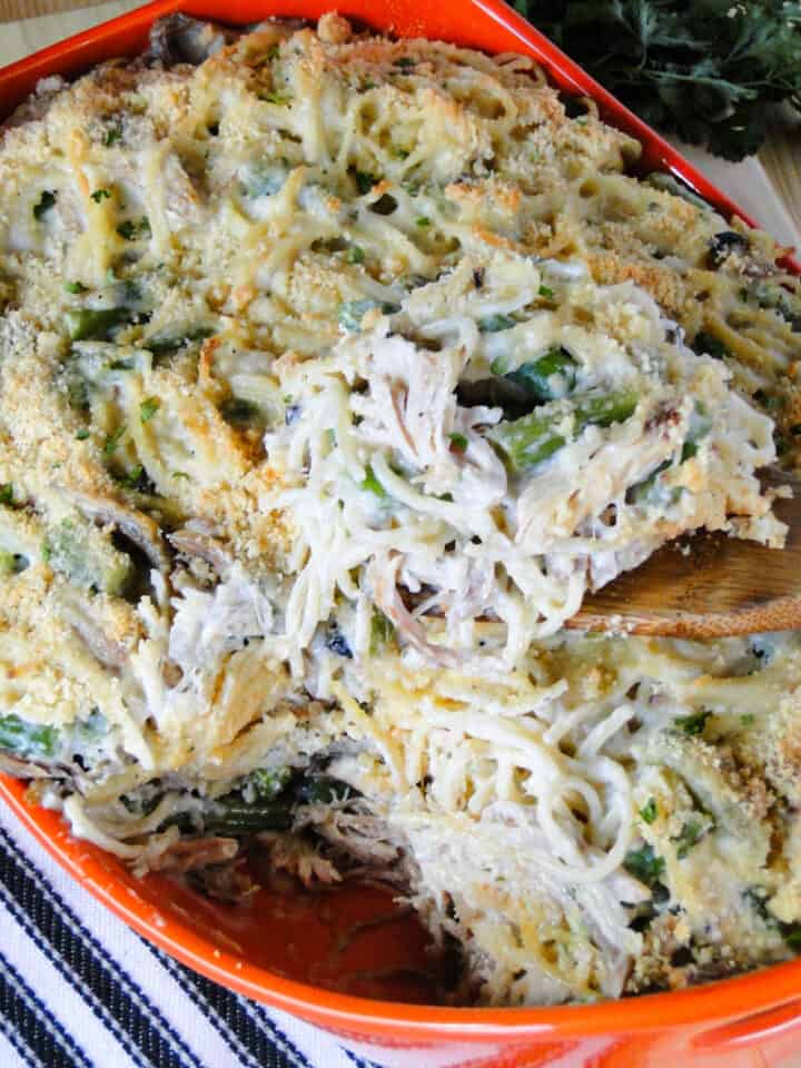Turkey tetrazzini being scooped out of casserole dish with wooden spoon.